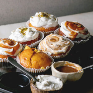 Orangen-Muffins mit Sahnehaube, Karamell-Swirl und Pistazien, dazu ein Muffin pur und eine Schale Karamell