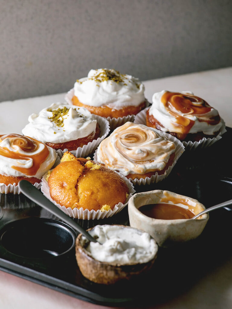 Orangen-Muffins mit Sahnehaube, Karamell-Swirl und Pistazien, dazu ein Muffin pur und eine Schale Karamell