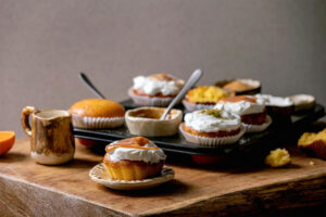 Fertige Orangen-Muffins mit verschiedenen Toppings auf einem Holzbrett: mit Sahnehaube, Pistazien und Karamell