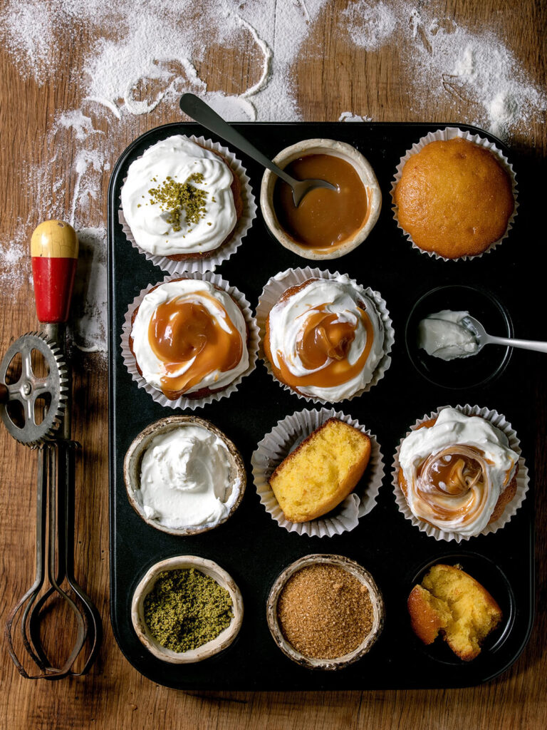 Orangen-Muffins von oben in verschiedenen Varianten: mit Sahnehaube, Pistazien, Karamell-Swirl und einer Schale Karamell