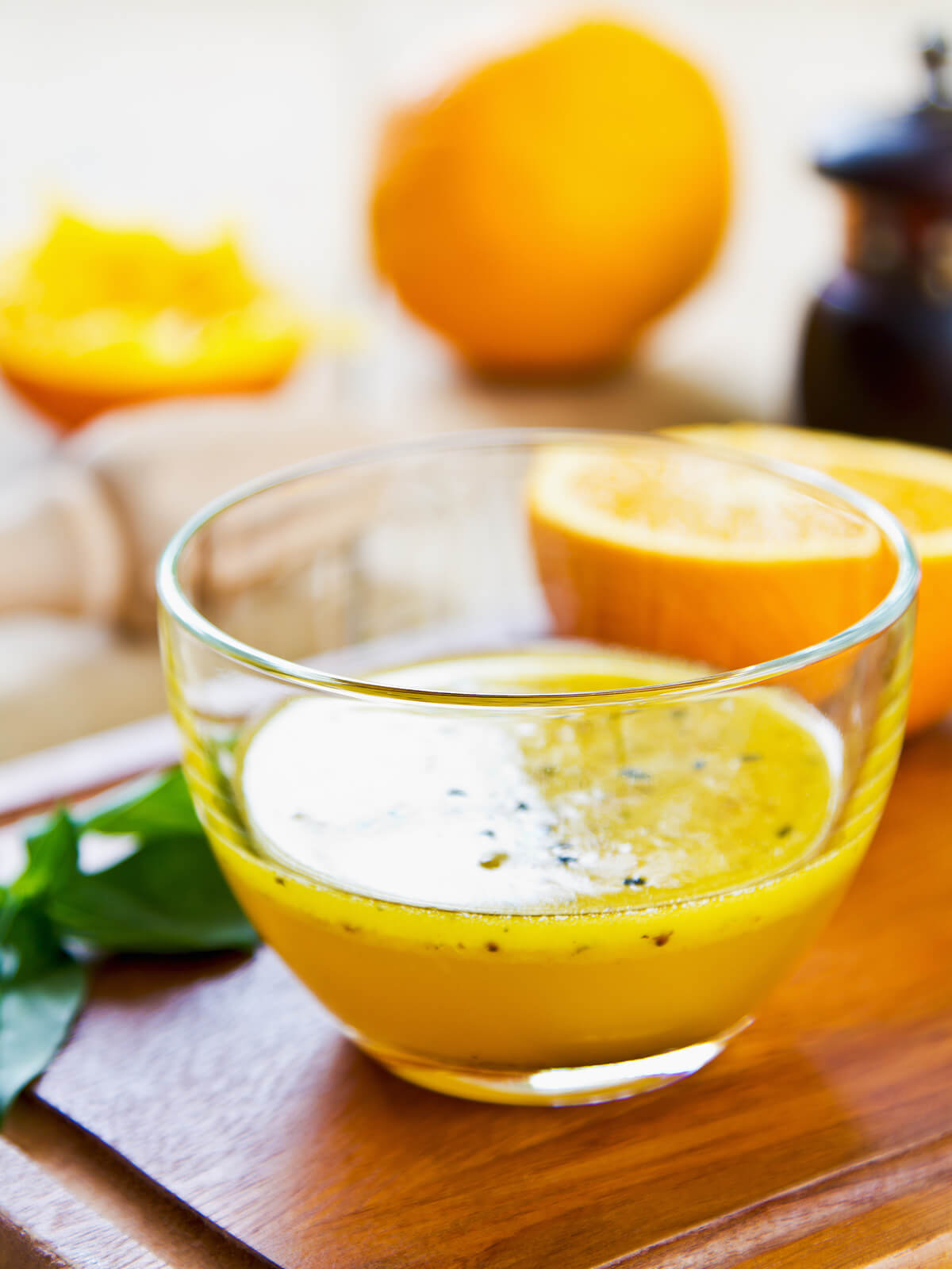 Goldorange Orangen-Vinaigrette mit schwarzem Sesam in einer Glasschale, daneben halbierte Orangen und Basilikum