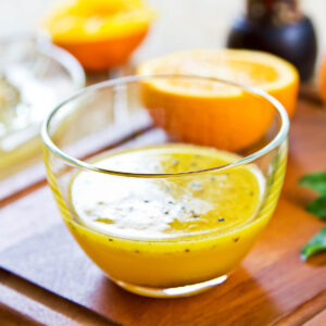 Orangen-Vinaigrette mit schwarzem Sesam in einer Glasschale, daneben eine ausgepresste Orange und eine Zitruspresse