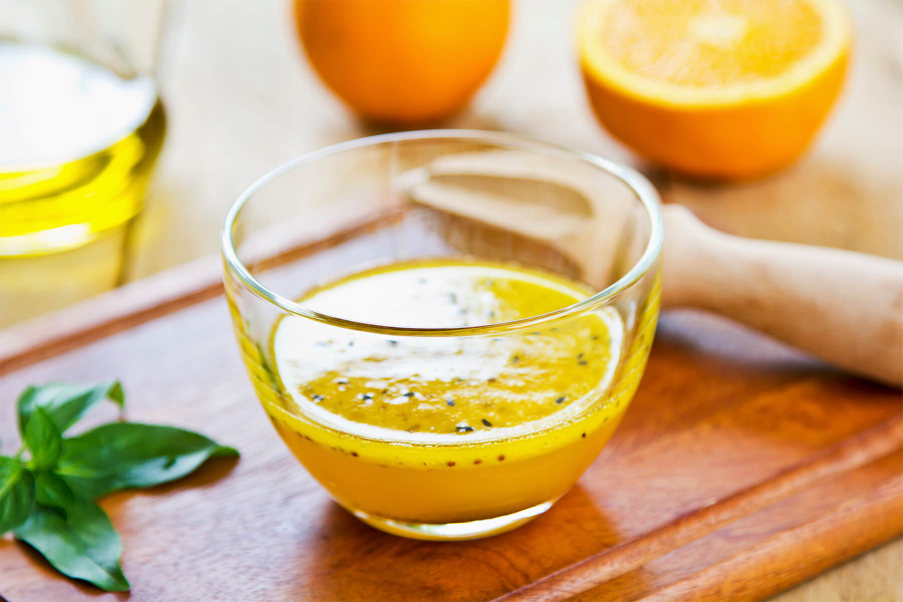 Orangen-Vinaigrette mit schwarzem Sesam in einer Glasschale mit frischem Basilikum und einer Ölflasche im Hintergrund