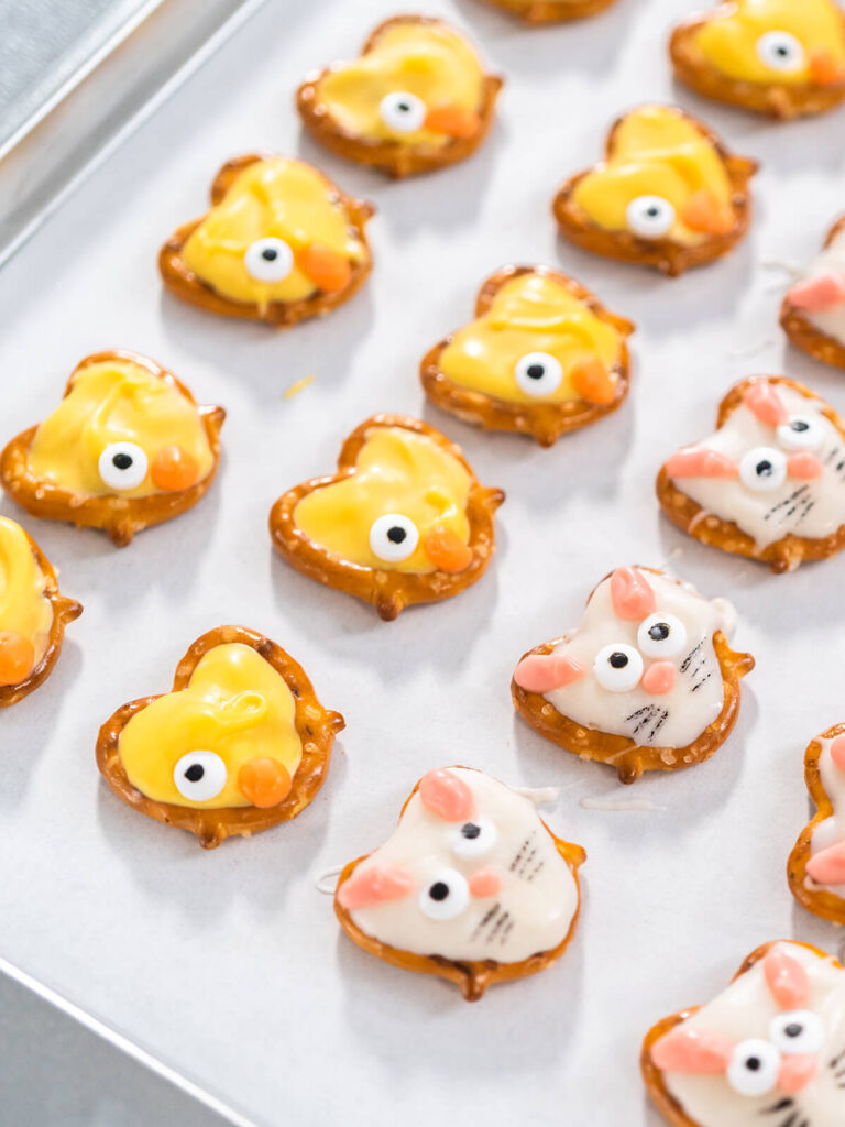 Fertige Oster-Schoko-Brezel als weiße Häschen und gelbe Küken auf hellem Backpapier von oben