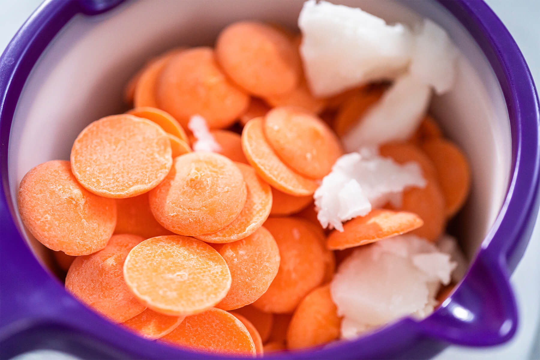Orange Schmelzdrops mit einem Stück Kokosöl in einem Schmelztopf, bereit zum langsamen Schmelzen