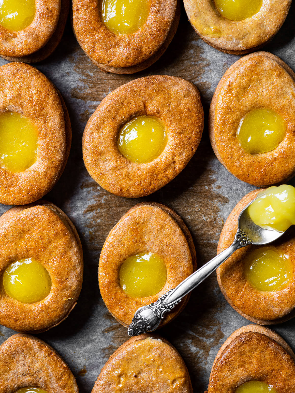 Osterei-Plätzchen mit Lemon Curd von oben auf Backpapier, dazu ein Löffel Zitronencreme