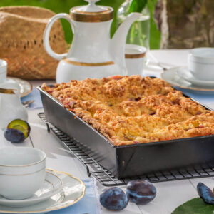Ganzer Pflaumen-Streuselkuchen mit dicker goldbrauner Streuselkrone in einer hohen rechteckigen Form auf einem Gitter im Garten
