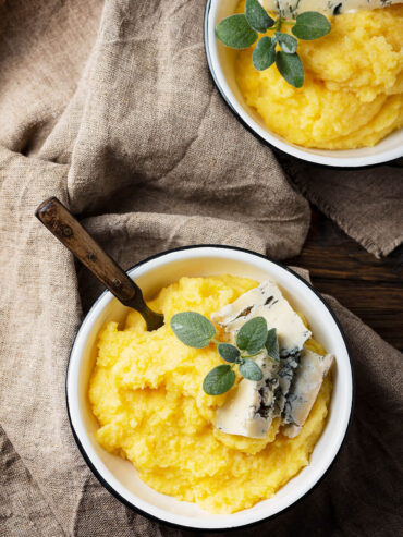 Zwei Schüsseln cremige Polenta mit Gorgonzola, frischem Salbei und Oregano, im Vordergrund eine Schüssel mit Löffel