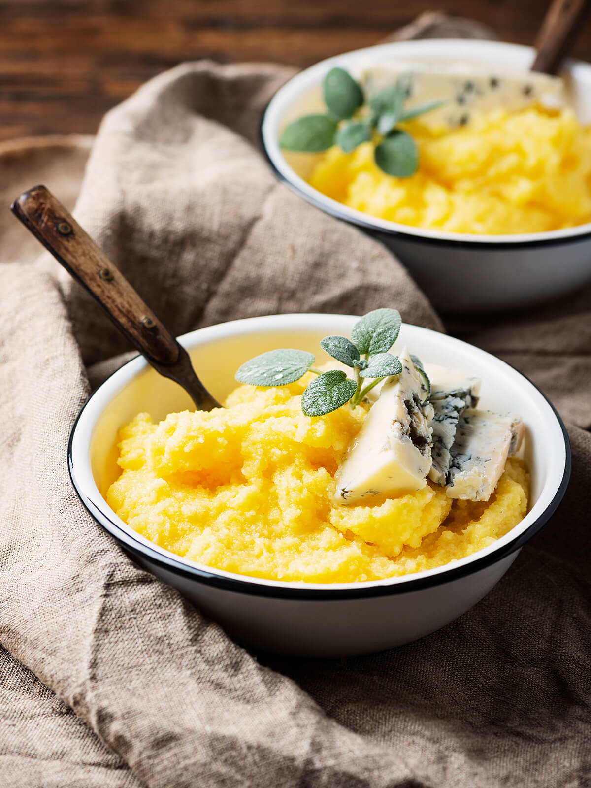 Zwei Schüsseln cremige Polenta mit Gorgonzola und frischen Kräutern auf einem Leinentuch