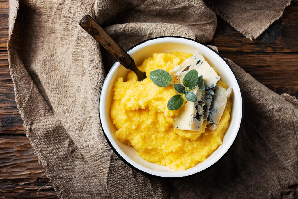 Cremige goldgelbe Polenta in einer Schüssel mit Gorgonzola-Stücken und frischem Salbei, von oben fotografiert