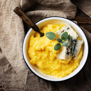 Cremige goldgelbe Polenta in einer Schüssel mit Gorgonzola-Stücken und frischem Salbei, von oben fotografiert