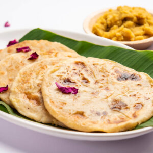 Goldbraune Puran Poli auf Bananenblatt mit einer Schale süßer Dal-Jaggery-Füllung, garniert mit Rosenblättern