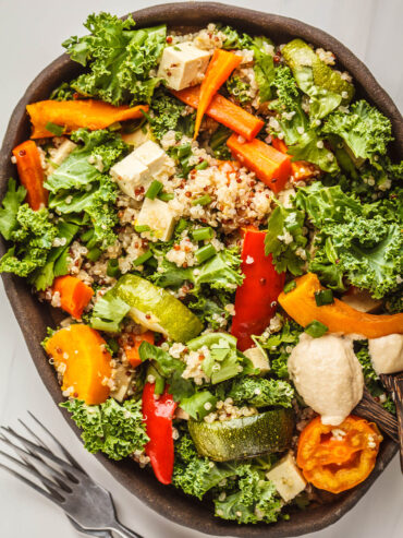 Vegane Quinoa-Bowl mit geröstetem Gemüse, Grünkohl, Tofu und Tahini-Dressing in einer dunklen Schale von oben
