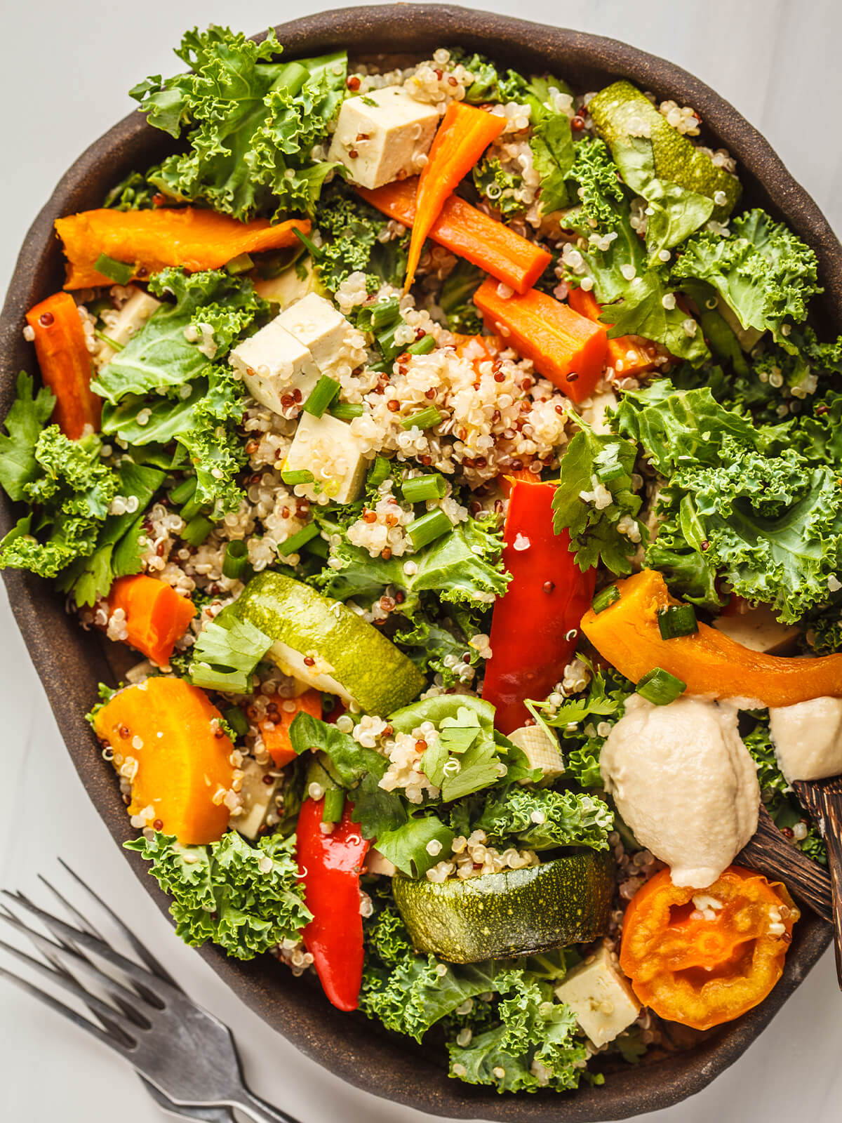 Vegane Quinoa-Bowl mit geröstetem Gemüse, Grünkohl, Tofu und Tahini-Dressing in einer dunklen Schale von oben