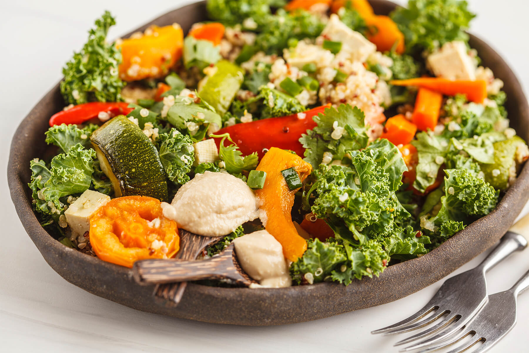 Nahaufnahme einer veganen Bowl mit geröstetem Gemüse, Grünkohl, Tofu und Tahini-Dressing in einer dunklen Schale