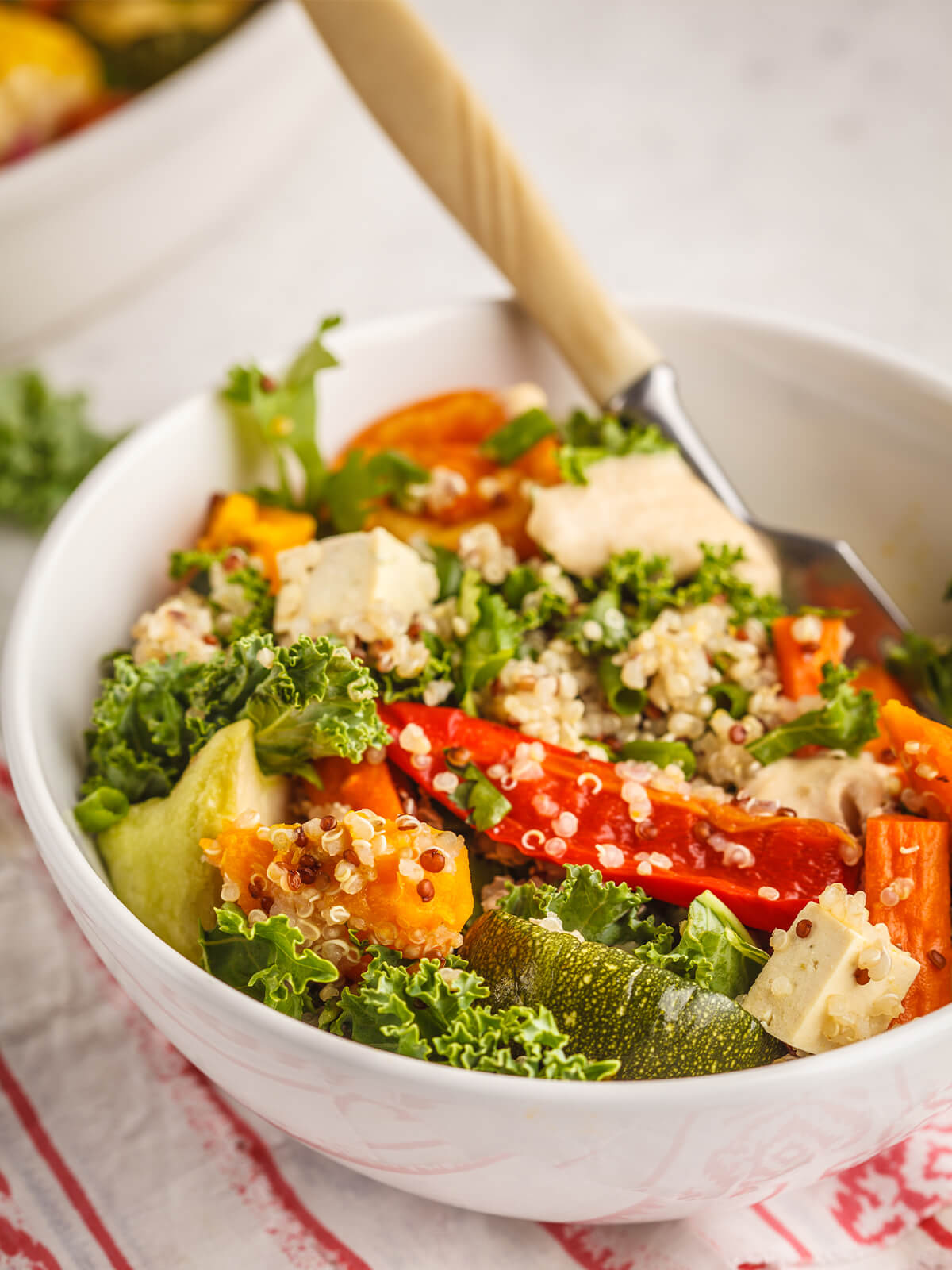 Vegane Quinoa-Bowl mit buntem Gemüse und Tofu in einer weißen Schale mit Gabel, seitlich fotografiert