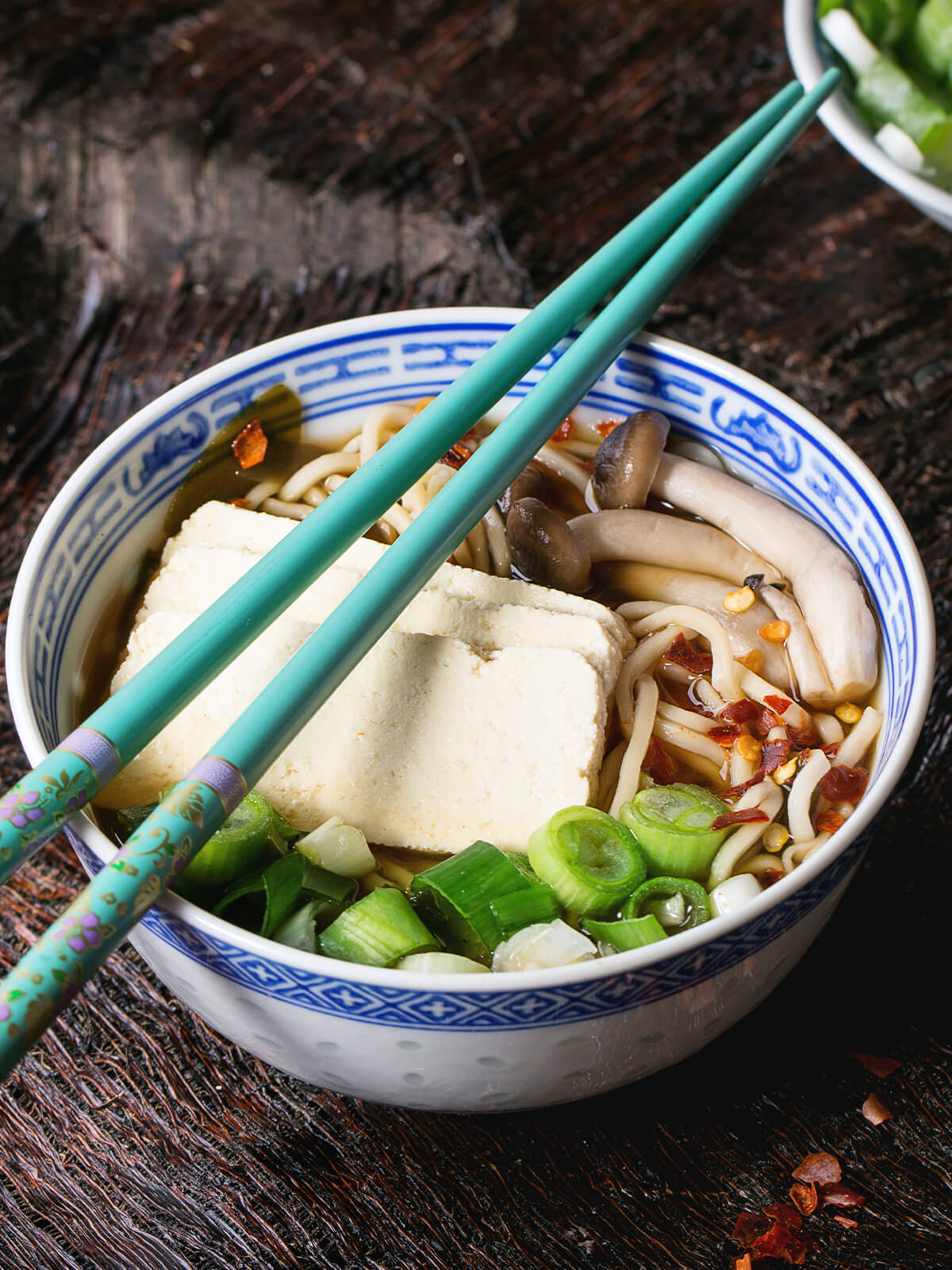 Vegetarische Ramen-Suppe mit Tofu, Pilzen und Nudeln in einer blau-weißen Schüssel, mit Frühlingszwiebeln und Chiliflocken