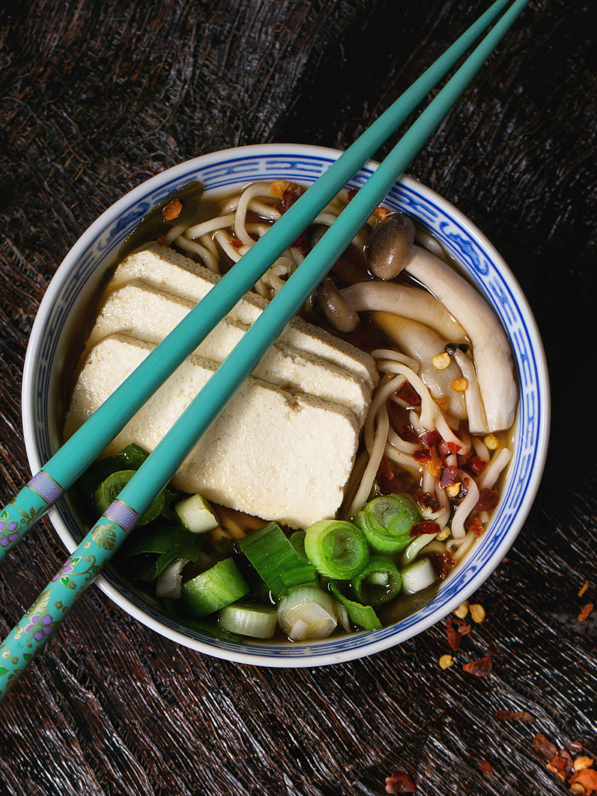 Ramen-Suppe von oben mit Tofu-Scheiben, Buchenpilzen, Austernpilzen, Nudeln, Kombu-Alge, Frühlingszwiebeln und Chiliflocken