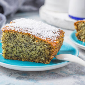 Ein Stück türkischer Grießkuchen mit Mohn (Revani), bestreut mit Kokosraspeln, auf einem türkisen Teller
