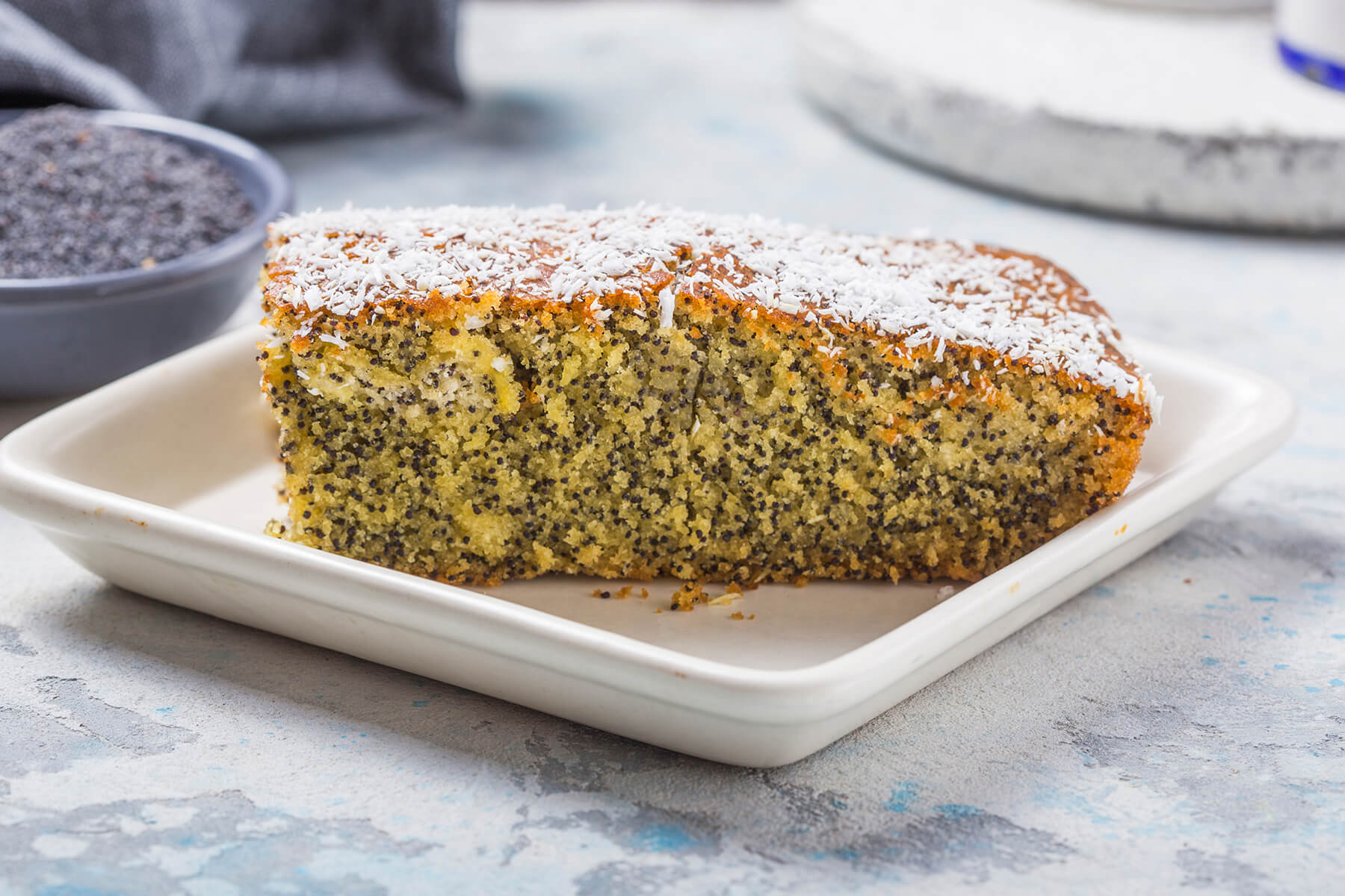 Ein Stück türkischer Grießkuchen mit Mohn (Revani) auf einem weißen Teller, mit Kokosraspeln bestreut
