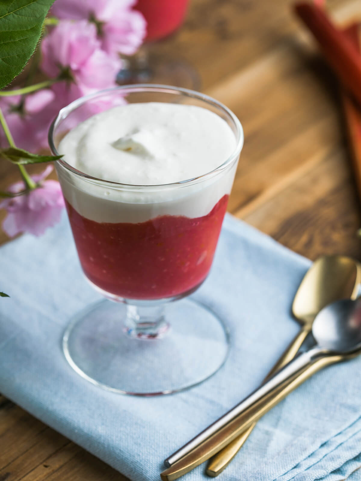 Rhabarber-Creme-Dessert im Glas mit roter Rhabarberschicht und weißer Vanille-Sahne-Creme, garniert mit Blüten