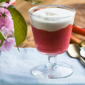 Rhabarber-Creme-Dessert im Glas mit roter Rhabarberschicht und weißer Vanille-Sahne-Creme, dekoriert mit Blüten