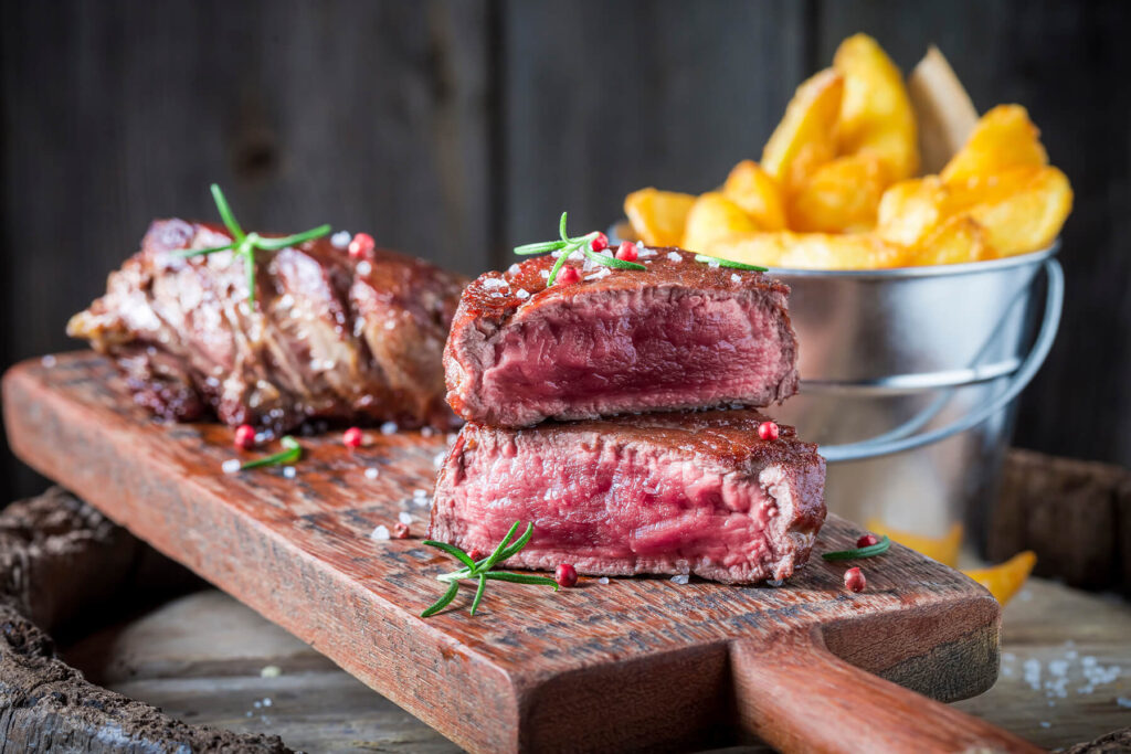 Steak medium rare aufgeschnitten mit rosa Kern, dazu knusprige Steakhouse-Pommes und Rosmarin