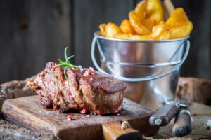 Gebratenes Steak mit Kruste und Rosmarin neben einem Becher knuspriger Steakhouse-Pommes