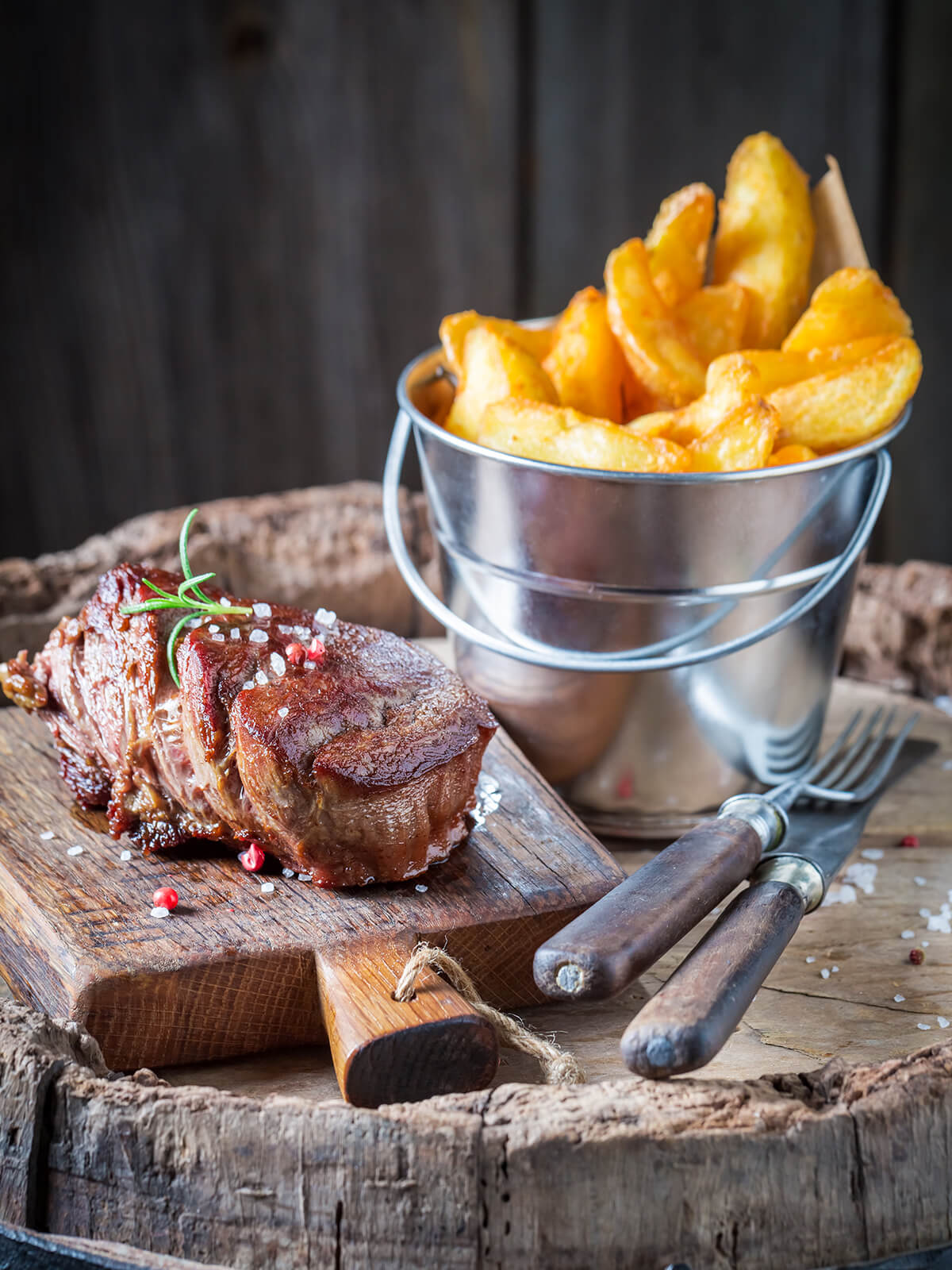 Gebratenes Steak mit Kruste und Rosmarin neben einem Becher knuspriger Steakhouse-Pommes