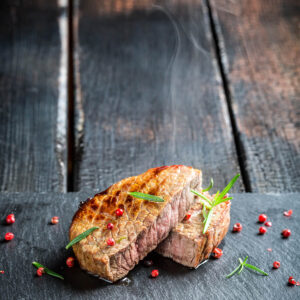 Gebratenes Rosmarin-Steak medium, aufgeschnitten mit rosa-grauem Kern, dazu Rosmarin und rosa Pfeffer auf Schiefer