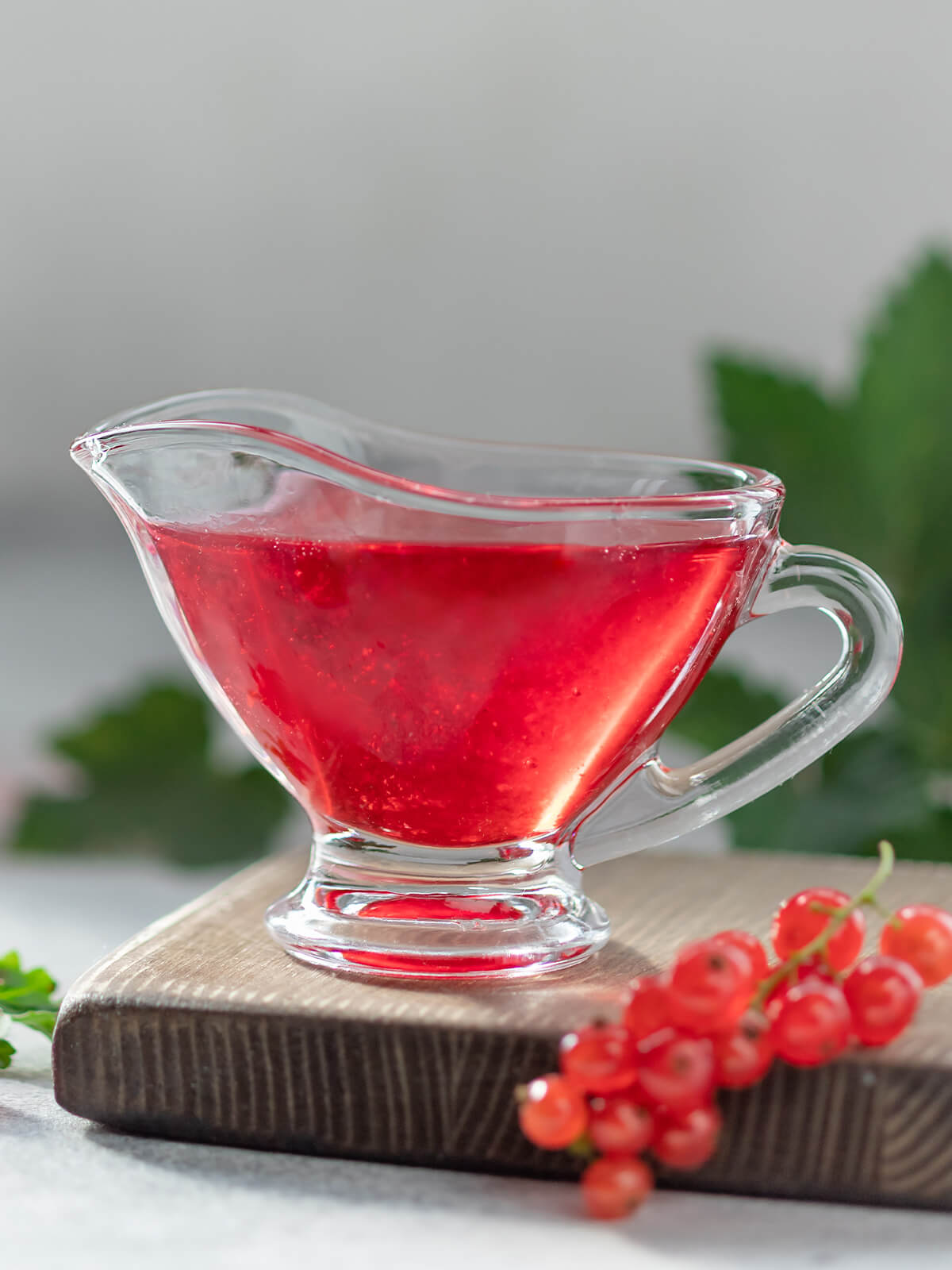 Klares rotes Johannisbeergelee in einer Glas-Sauciere, daneben frische rote Johannisbeeren