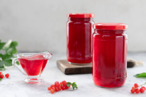 Zwei Gläser mit fertigem klarem roten Johannisbeergelee und eine Sauciere mit Gelee, daneben frische Johannisbeeren