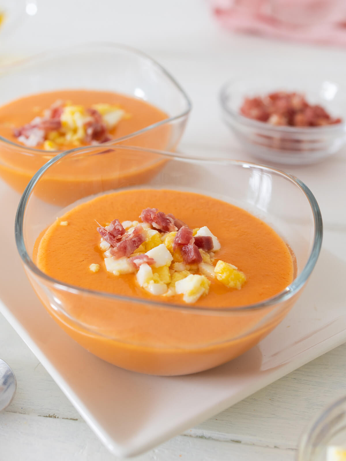 Nahaufnahme zweier Glasschälchen mit cremigem orangerotem Salmorejo, getoppt mit gewürfeltem Serrano-Schinken und gehacktem Ei