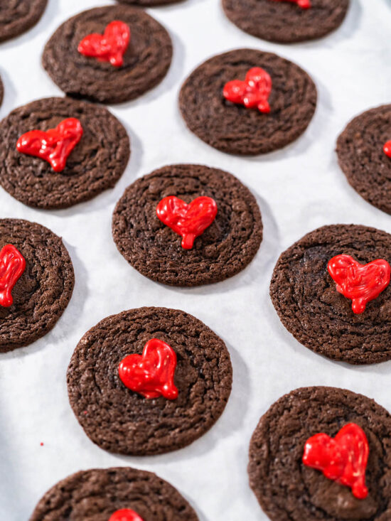 Mehrere weiche Schokoladen-Cookies mit glänzenden roten Schoko-Herzen von oben