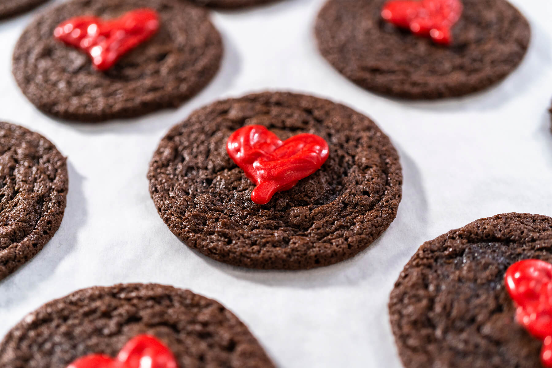 Schokoladen-Cookies mit roten Schoko-Herzen auf Backpapier angerichtet