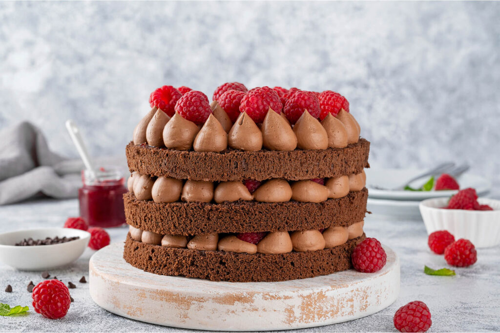 Schoko-Himbeer-Torte mit drei Schokoladenbiskuits, aufgespritzten Schokocreme-Tupfen und frischen Himbeeren im Naked-Cake-Look