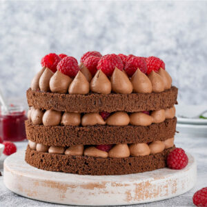Schoko-Himbeer-Torte mit drei Schokoladenbiskuits, aufgespritzten Schokocreme-Tupfen und frischen Himbeeren im Naked-Cake-Look