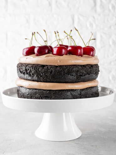 Schoko-Kirsch-Torte im Naked-Cake-Look mit zwei dunklen Schokoladenböden, luftiger Schokosahne und frischen Kirschen auf einer weißen Tortenplatte
