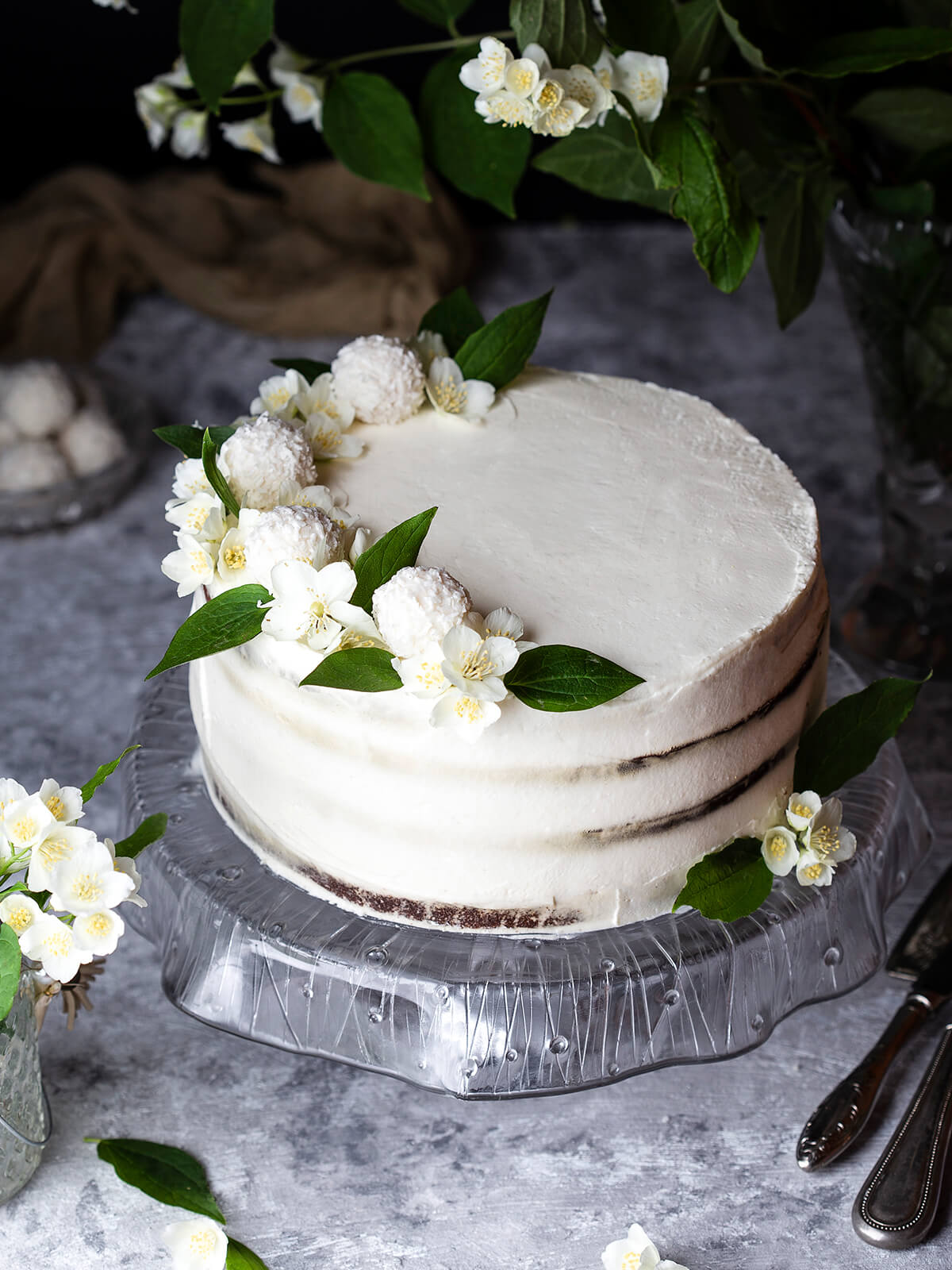 Schoko-Kokos-Torte schräg von oben mit weißen Blüten, Kokoskugeln und grünen Blättern auf dunklem Hintergrund