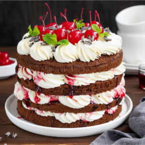 Klassische Schwarzwälder Kirschtorte im Naked-Cake-Look mit dunklen Schokoladenböden, weißer Sahne, Sauerkirschen, Schokoraspeln und Cocktailkirschen