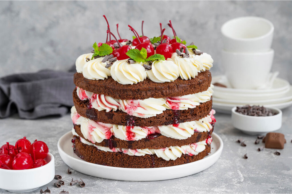 Fertige Schwarzwälder Kirschtorte mit Sahnetuffs, Schokoraspeln, Cocktailkirschen und Minze auf einem weißen Teller