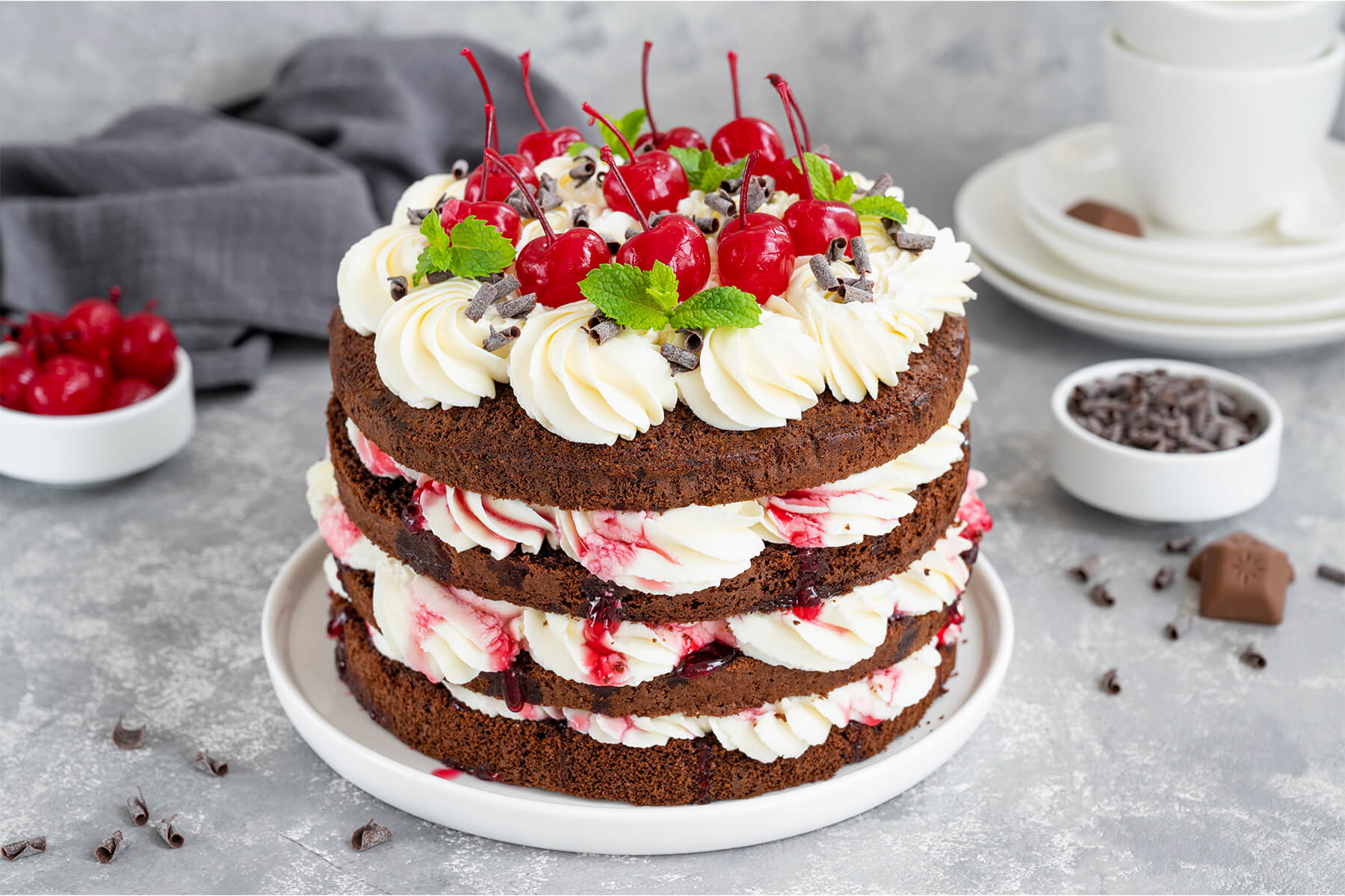 Schwarzwälder Kirschtorte im Naked-Cake-Look von der Seite mit vier dunklen Schokoladenböden, weißen Sahneschichten und roten Sauerkirschen dazwischen