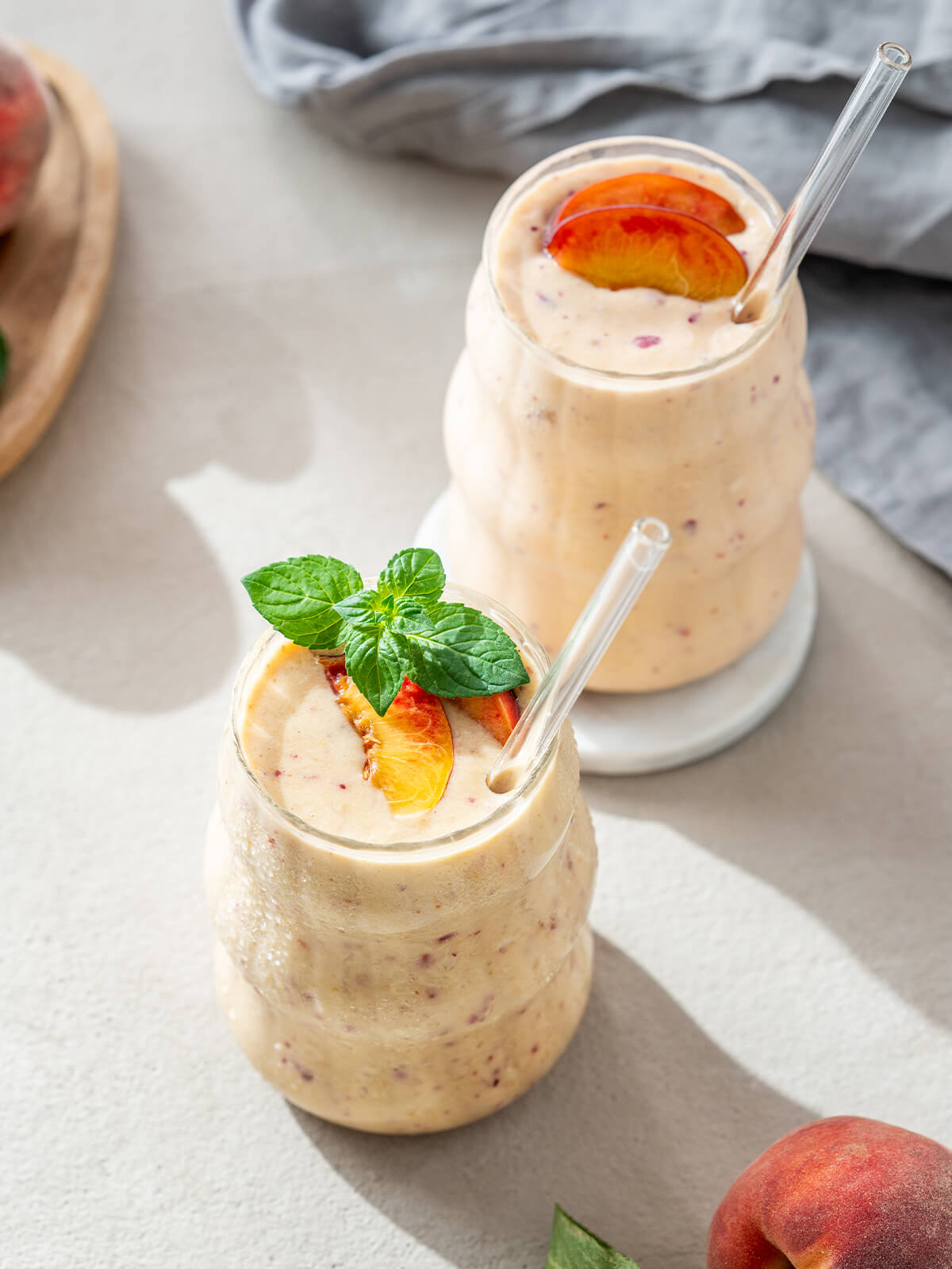 Zwei Gläser Pfirsich-Bananen-Smoothie von oben mit Minze und Pfirsichspalten garniert