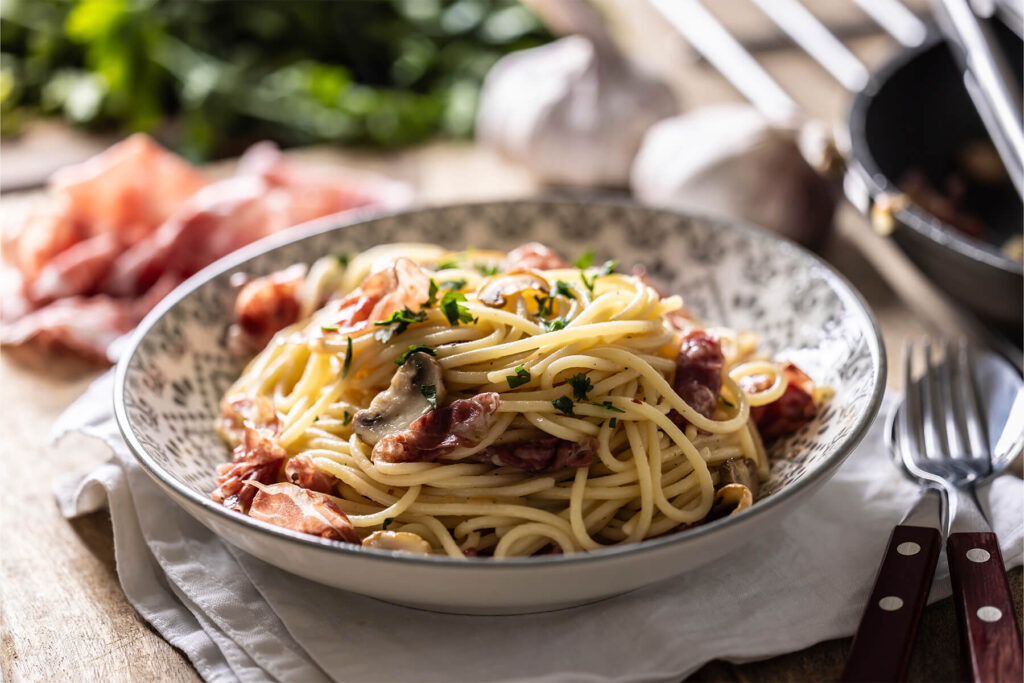 Nahaufnahme von Spaghetti mit Prosciutto, Champignons, Parmesan und Petersilie in einer gemusterten Schale