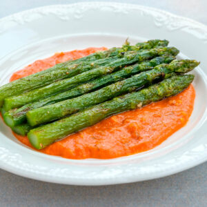 Gebratener grüner Spargel mit Röstaromen auf einem Spiegel aus orangeroter Romesco-Sauce auf weißem Teller