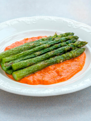 Gebratener grüner Spargel mit Röstaromen auf einem Spiegel aus orangeroter Romesco-Sauce auf weißem Teller
