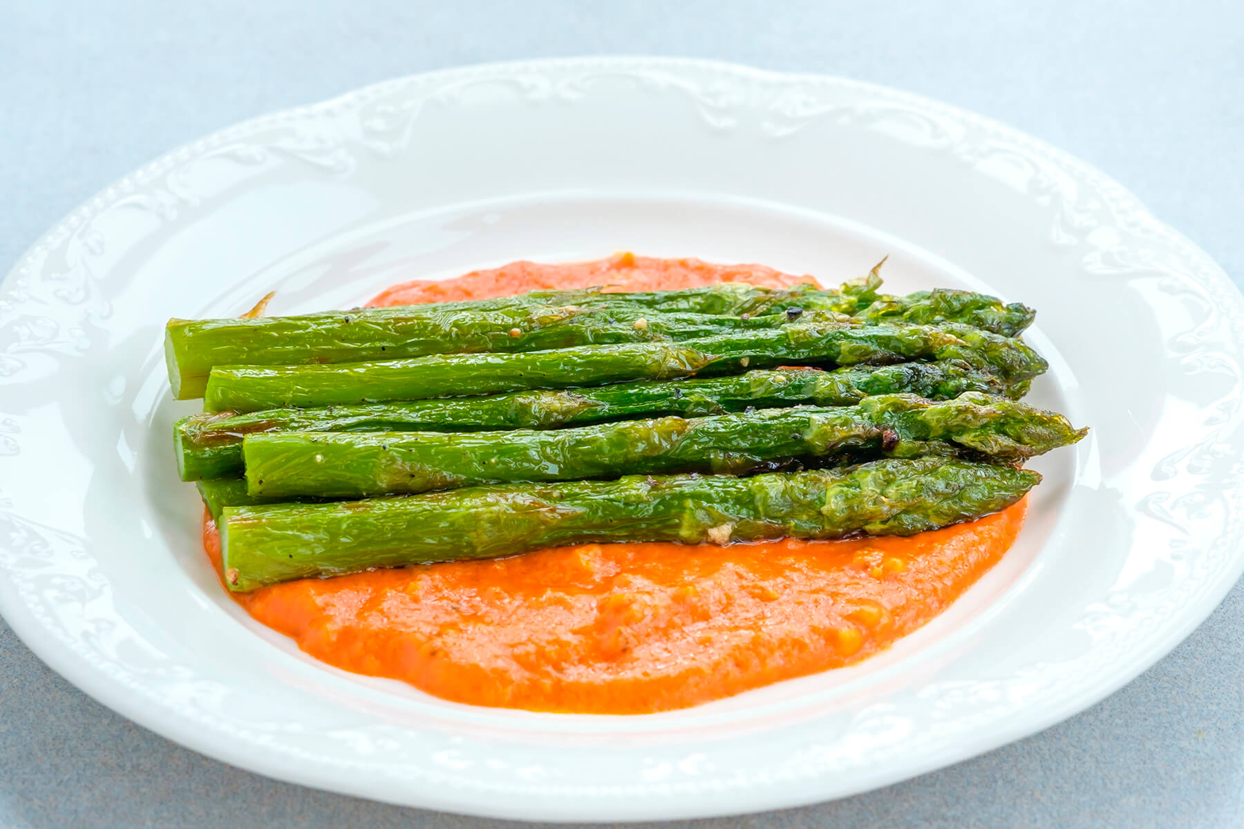 Nahaufnahme der samtigen orangeroten Romesco-Sauce mit gebratenem grünem Spargel darauf