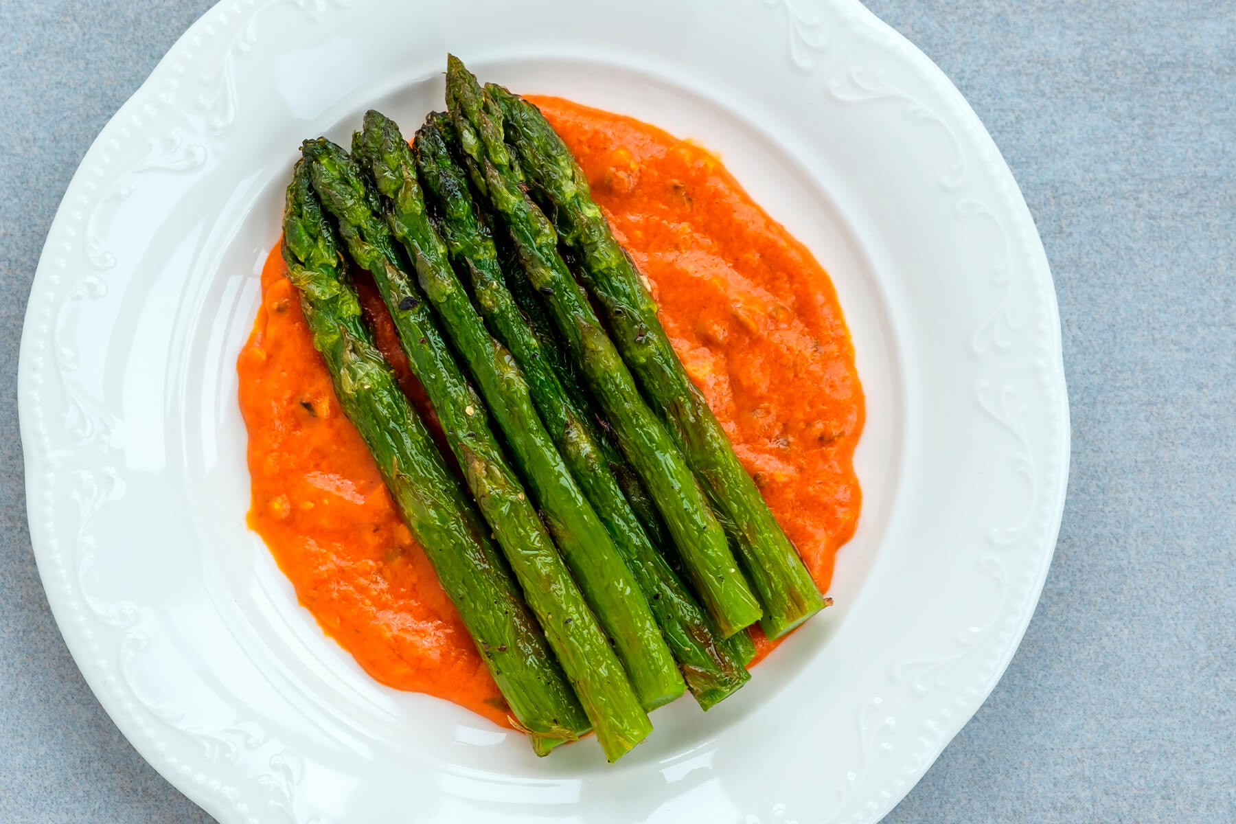 Gebratener grüner Spargel von oben auf einem Spiegel aus Romesco-Sauce auf weißem Teller