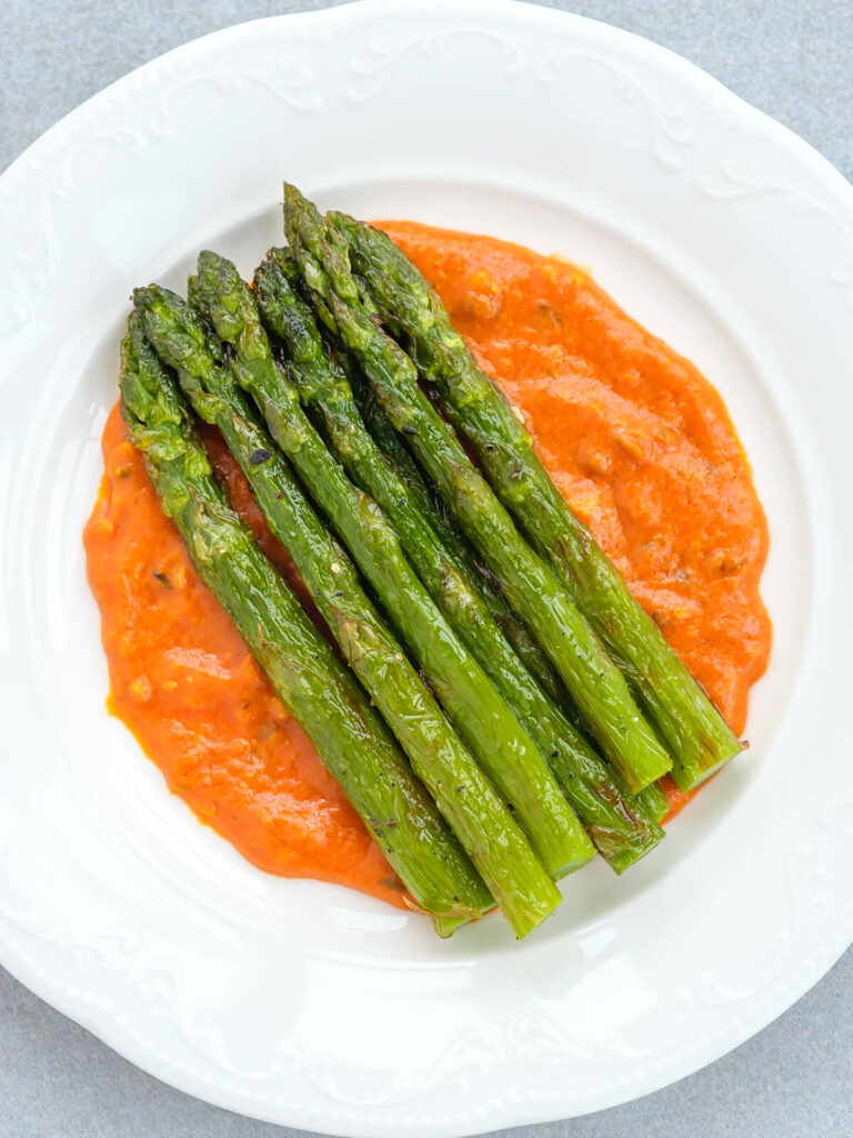 Gebratener grüner Spargel mit Röstaromen auf einem Spiegel aus orangeroter Romesco-Sauce