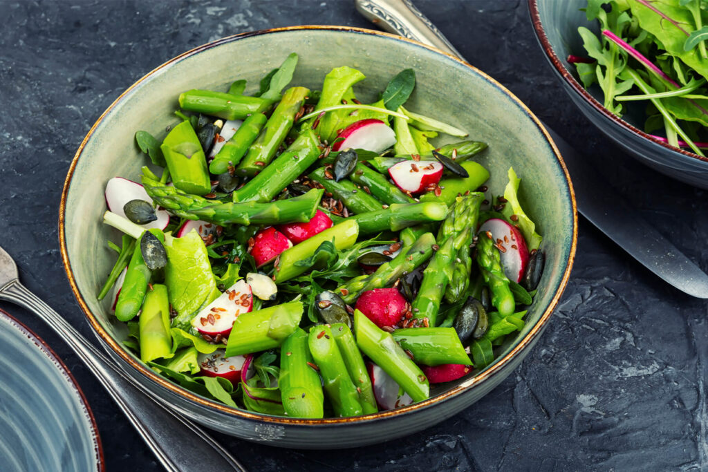 Grüner Spargelsalat mit Radieschen, Blattsalat, Kürbiskernen und Leinsamen in einer Schüssel